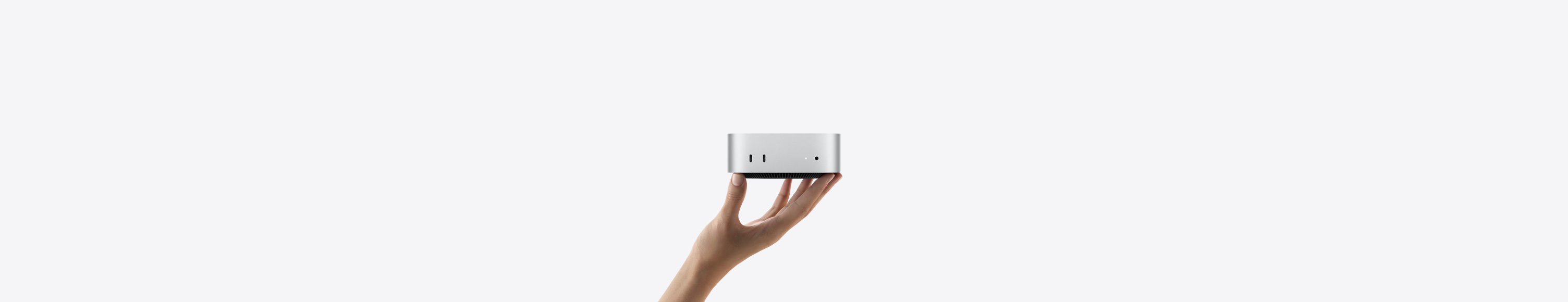 向上展開的手，指尖上平衡地立著一部銀色 Mac mini，機身朝前，正面秀出兩個 Thunderbolt 埠、狀態指示燈與耳機插孔、底端收窄設計的黑色底座、平坦的頂端、圓角側邊與平直的機身邊緣
