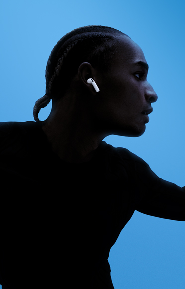 En person med AirPods 5 i ørerne og armene bredt ud mod en baggrund i flere farver