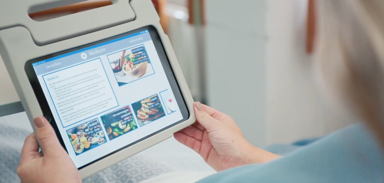 Una paciente mira la pantalla de un iPad mientras está sentada en su cama de hospital.